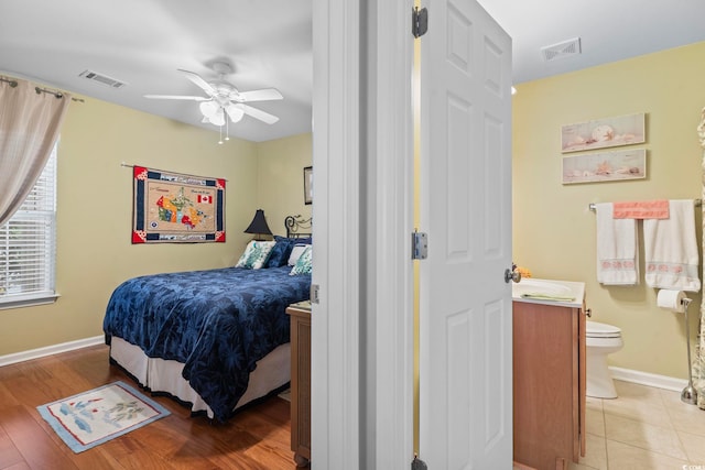 bedroom featuring light tile patterned flooring, visible vents, ensuite bath, and baseboards