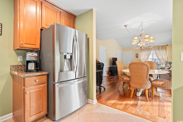 kitchen with light stone countertops, stainless steel fridge with ice dispenser, vaulted ceiling, light tile patterned floors, and a notable chandelier