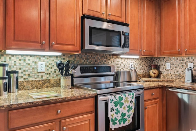 kitchen with light stone counters, tasteful backsplash, appliances with stainless steel finishes, and brown cabinets