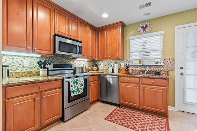 kitchen with visible vents, stone counters, a sink, stainless steel appliances, and brown cabinets