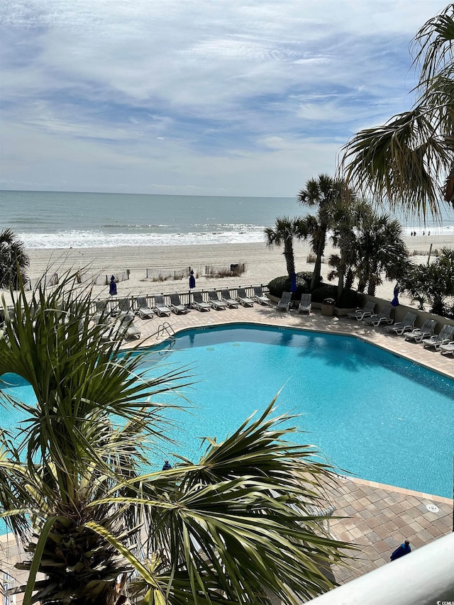 community pool featuring a water view, a patio, and a view of the beach