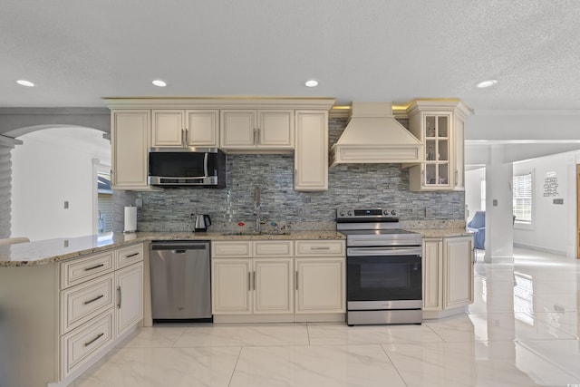 3763 Annandale Dr, Myrtle Beach, SC 29577 - kitchen with custom range hood, appliances with stainless steel finishes, arched walkways, cream cabinetry, and a sink