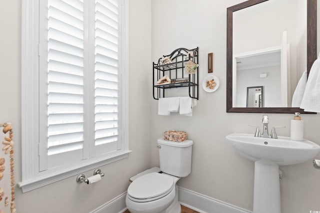 half bath with toilet, baseboards, and a sink