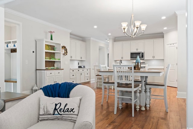 kitchen with light wood-style flooring, ornamental molding, white cabinets, stainless steel microwave, and a chandelier