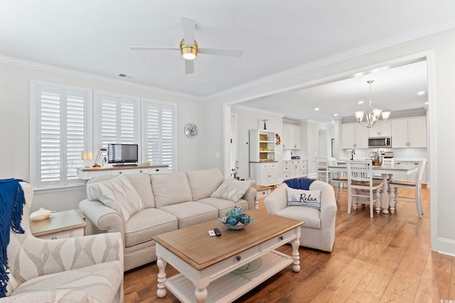 living room featuring visible vents, ceiling fan with notable chandelier, crown molding, and light wood finished floors