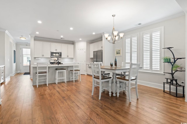 dining space featuring baseboards, a chandelier, ornamental molding, and light wood finished floors