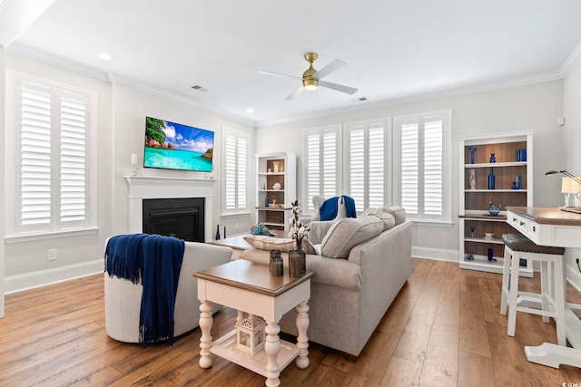 living area with hardwood / wood-style floors, visible vents, baseboards, ceiling fan, and crown molding