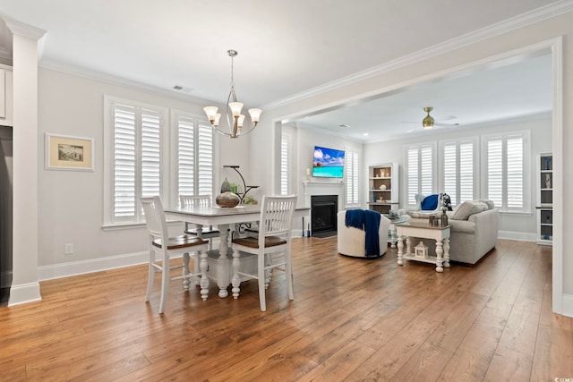 dining area featuring light wood-style flooring, ornamental molding, ceiling fan with notable chandelier, a fireplace, and baseboards