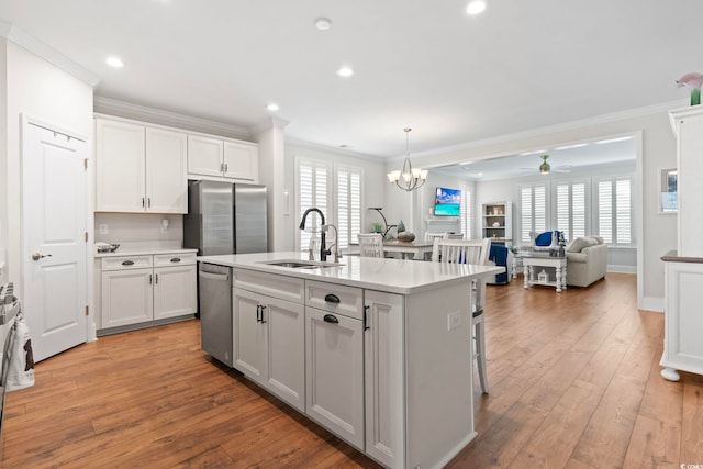 kitchen with ornamental molding, a sink, appliances with stainless steel finishes, ceiling fan with notable chandelier, and light wood-type flooring