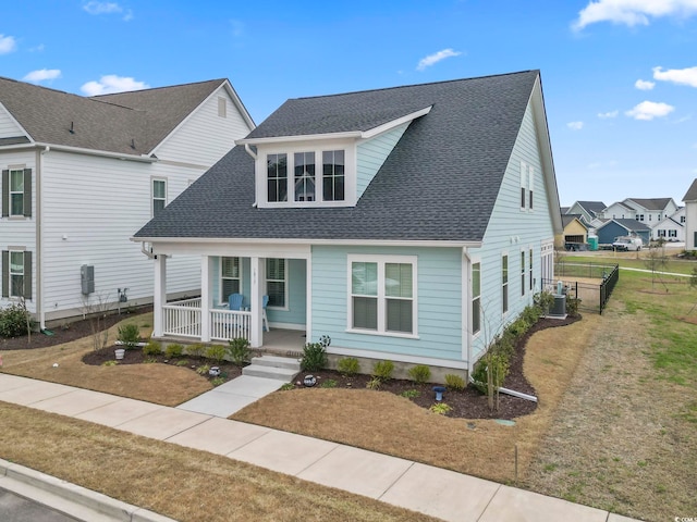 view of front of house with covered porch, cooling unit, a front lawn, and roof with shingles