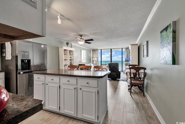 kitchen featuring wood finish floors, expansive windows, a textured ceiling, stainless steel fridge with ice dispenser, and crown molding