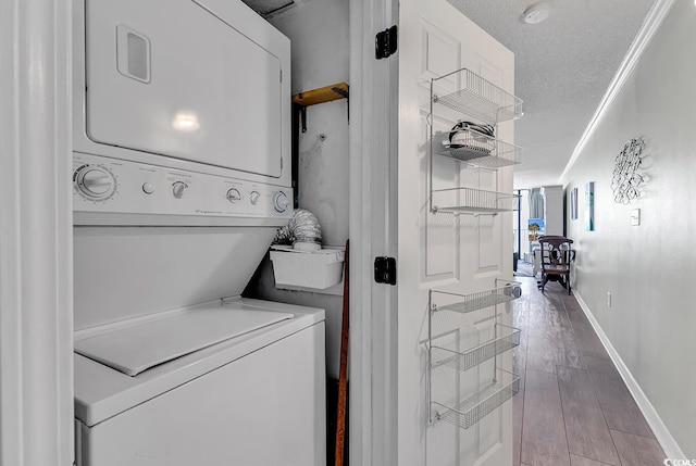 laundry area with crown molding, stacked washer and dryer, laundry area, wood finished floors, and a textured ceiling