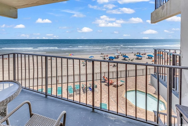 balcony featuring a jacuzzi, a water view, and a view of the beach