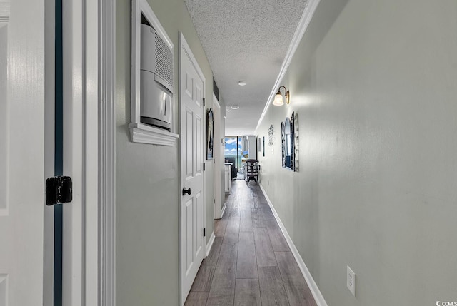 hall with baseboards, a textured ceiling, wood finished floors, and ornamental molding