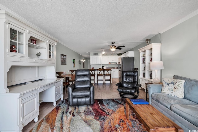 living room with wood finished floors, a textured ceiling, ceiling fan, and ornamental molding