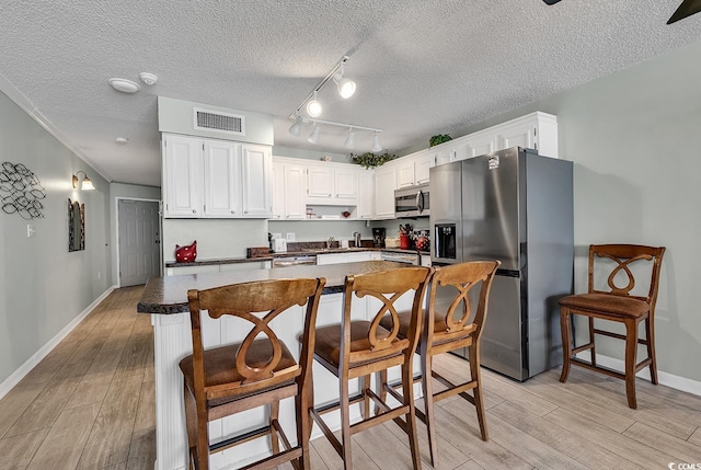 kitchen with dark countertops, visible vents, light wood-style flooring, and appliances with stainless steel finishes