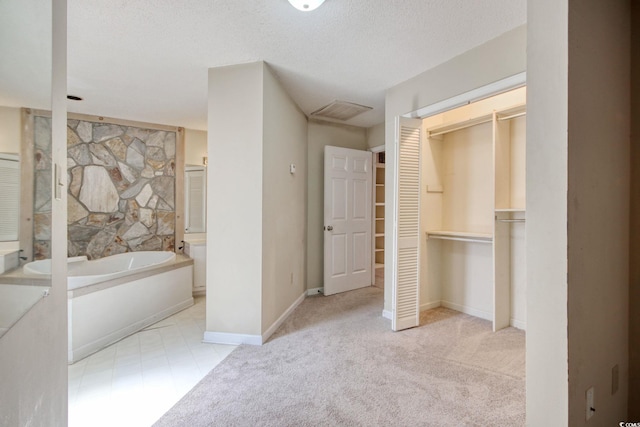 full bathroom featuring visible vents, a walk in closet, a garden tub, a textured ceiling, and baseboards