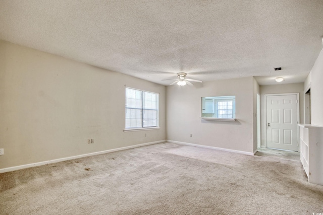 carpeted spare room featuring a textured ceiling, visible vents, baseboards, and ceiling fan