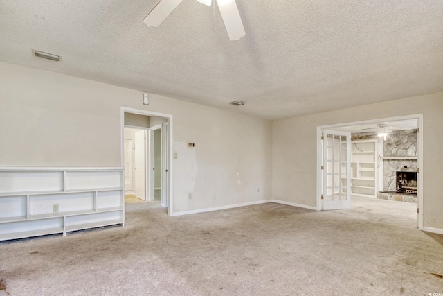 carpeted spare room featuring a stone fireplace, a textured ceiling, baseboards, and ceiling fan