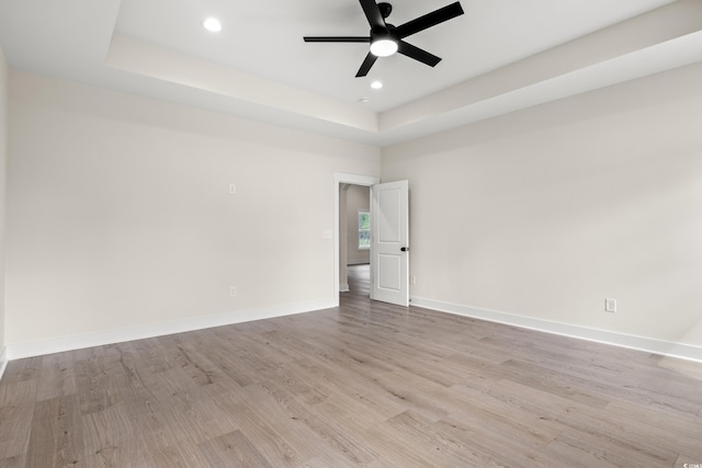 spare room with a raised ceiling, light wood-style flooring, a ceiling fan, recessed lighting, and baseboards