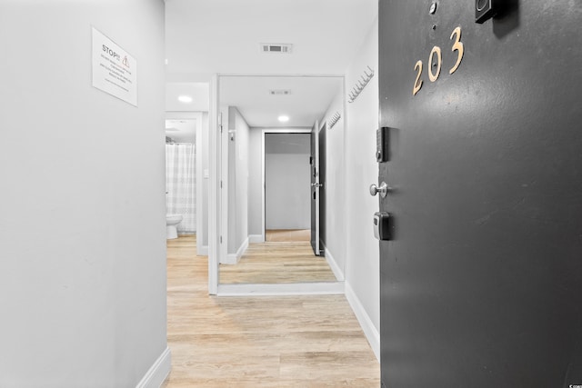 hallway featuring visible vents, baseboards, and light wood finished floors