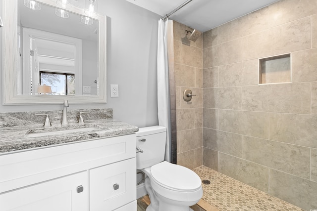 bathroom with toilet, tiled shower, and vanity