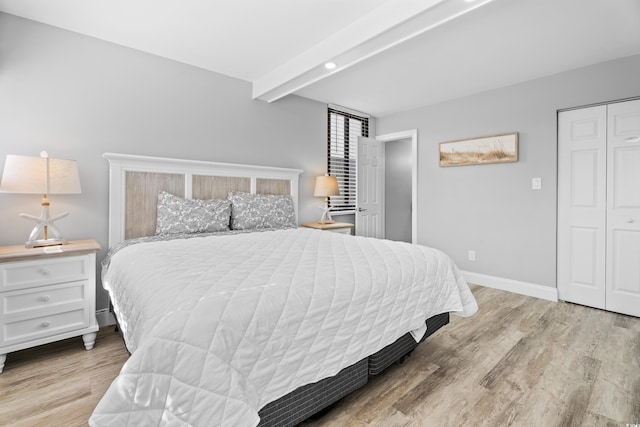 bedroom with beamed ceiling, wood finished floors, baseboards, and a closet