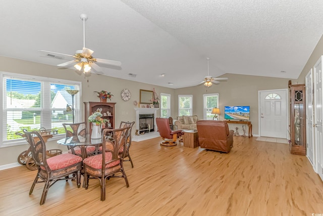 dining space featuring ceiling fan, lofted ceiling, a fireplace, light wood-style floors, and a textured ceiling