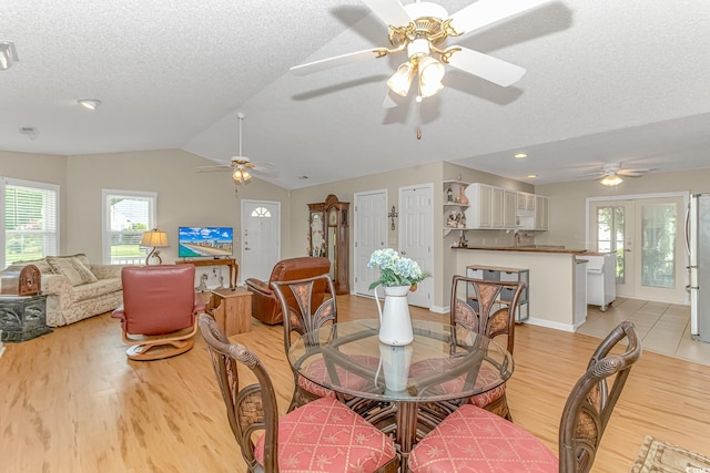 dining room with a textured ceiling, lofted ceiling, light wood-type flooring, and ceiling fan