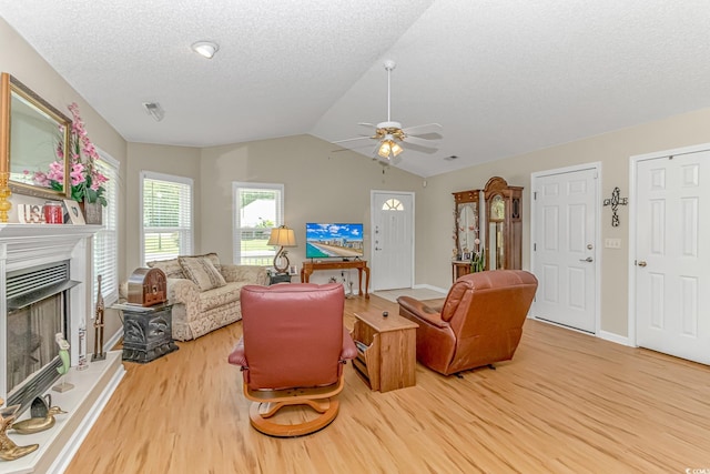 living area featuring vaulted ceiling, a fireplace with raised hearth, ceiling fan, and wood finished floors