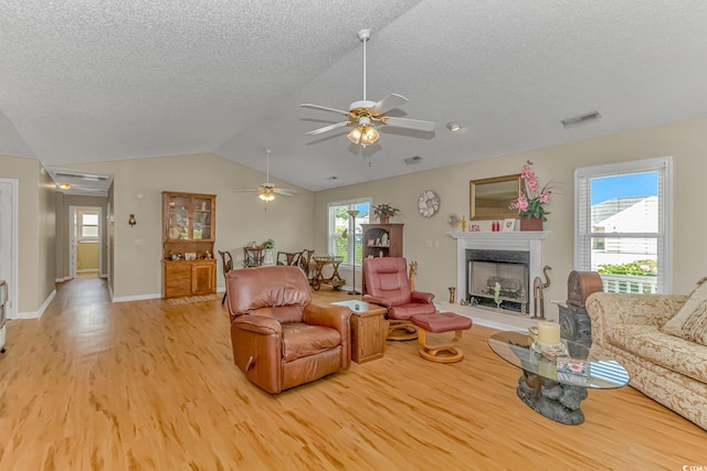 living area with a high end fireplace, visible vents, light wood-type flooring, vaulted ceiling, and a ceiling fan