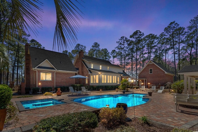 pool at dusk featuring an outdoor pool, an in ground hot tub, and a patio