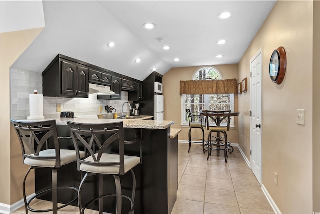 kitchen featuring tasteful backsplash, under cabinet range hood, lofted ceiling, light tile patterned flooring, and a sink