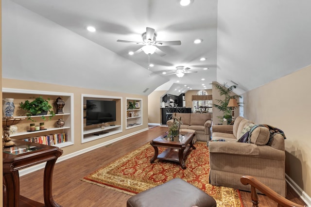 living area featuring built in features, wood finished floors, baseboards, ceiling fan, and vaulted ceiling