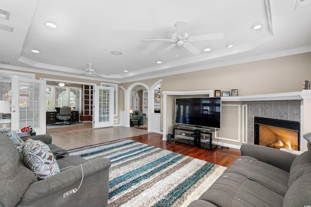 living area with a tray ceiling, wood finished floors, french doors, a fireplace, and ceiling fan