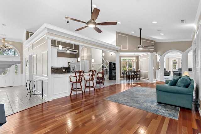 living room featuring hardwood / wood-style floors, stairway, ornate columns, arched walkways, and ceiling fan with notable chandelier