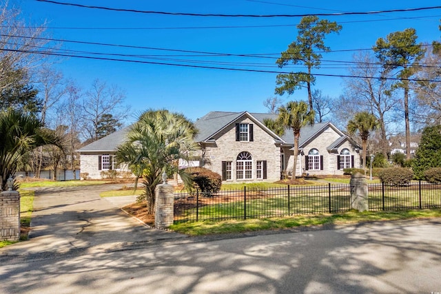 view of front of property featuring a fenced front yard, stone siding, driveway, and a front lawn