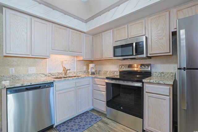 kitchen featuring appliances with stainless steel finishes, a sink, light wood-type flooring, light stone counters, and backsplash