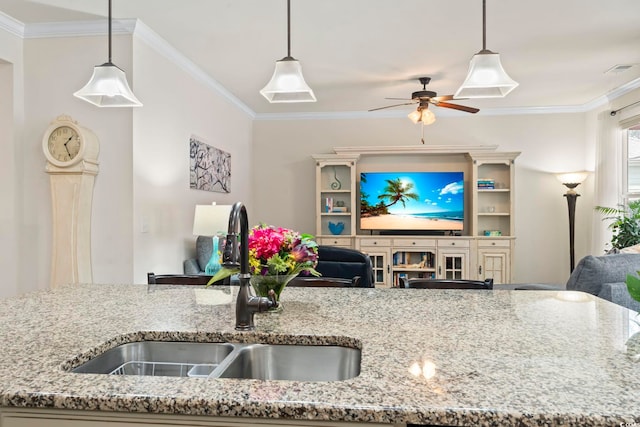 kitchen with a sink, open floor plan, crown molding, light stone countertops, and ceiling fan