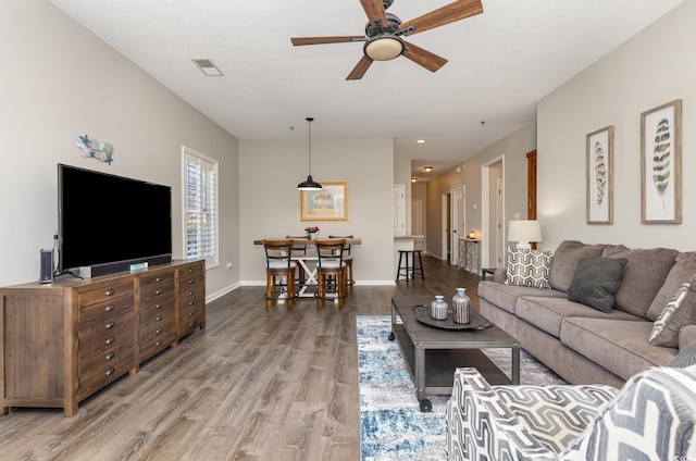 living area featuring visible vents, light wood-style flooring, baseboards, and ceiling fan