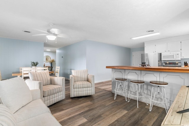 living area featuring a ceiling fan, visible vents, dark wood-style flooring, and baseboards