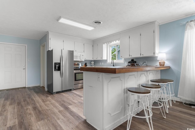 kitchen featuring visible vents, a peninsula, appliances with stainless steel finishes, wood counters, and white cabinetry