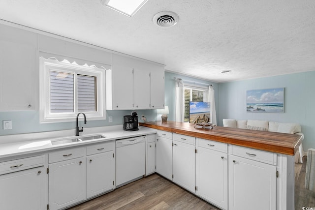 kitchen featuring visible vents, light wood-style flooring, a sink, a peninsula, and dishwasher