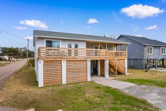 coastal home featuring stairs, a deck, a front lawn, and a shingled roof