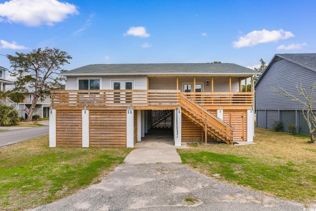 view of front of property featuring a front lawn, driveway, a shingled roof, a wooden deck, and stairs