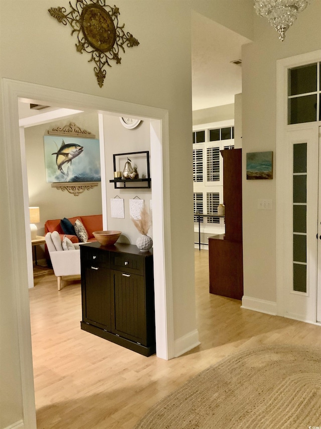 corridor featuring a notable chandelier, baseboards, and light wood finished floors