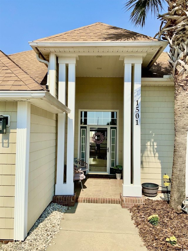 view of exterior entry featuring covered porch and roof with shingles