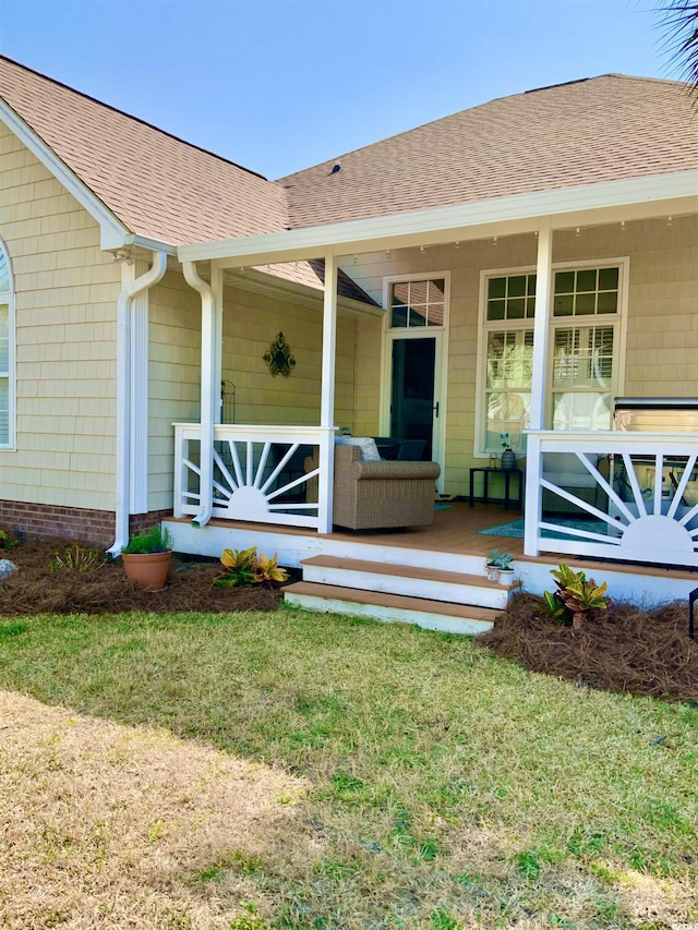 doorway to property featuring a porch, a lawn, and roof with shingles