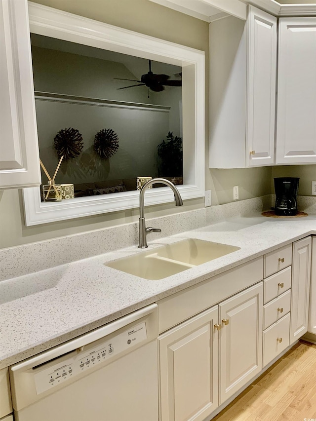 kitchen with a sink, light stone counters, light wood-style floors, and white dishwasher