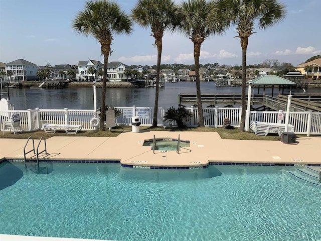 community pool featuring a hot tub, a water view, a patio, and fence